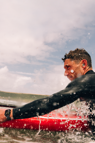 A man with a paddle board in the water wearing an Apple Watch Series 10.